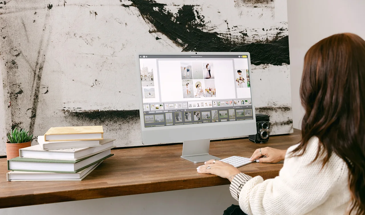 A designer at a desk laying out album spreads on a large monitor