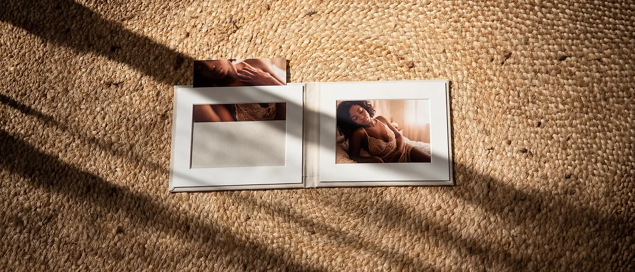 A lay-flat boudoir album open flat on a woven rug in low afternoon light