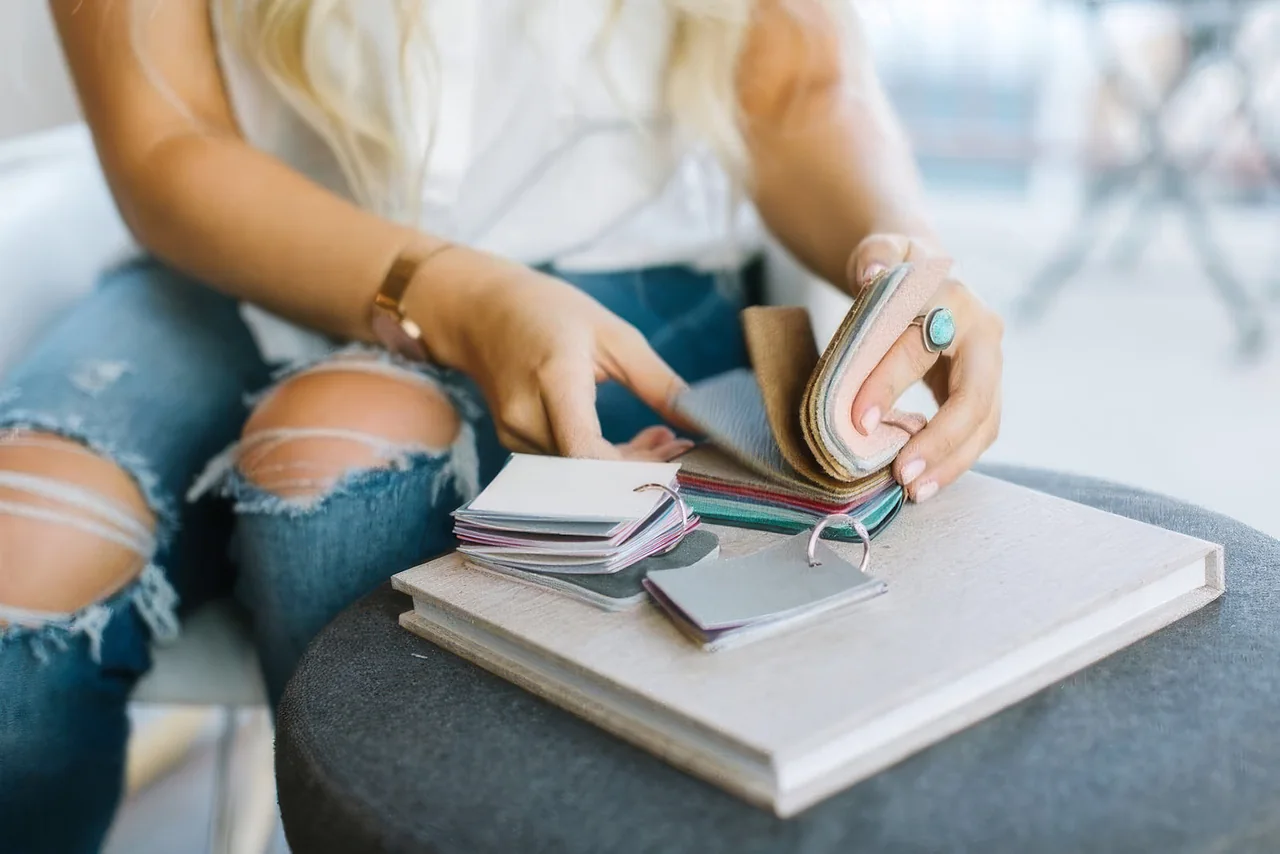 Somebody smiling behind a stack of linen-bound albums in different colours