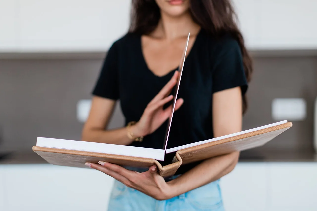 A person holding an open album whose pages lie perfectly flat