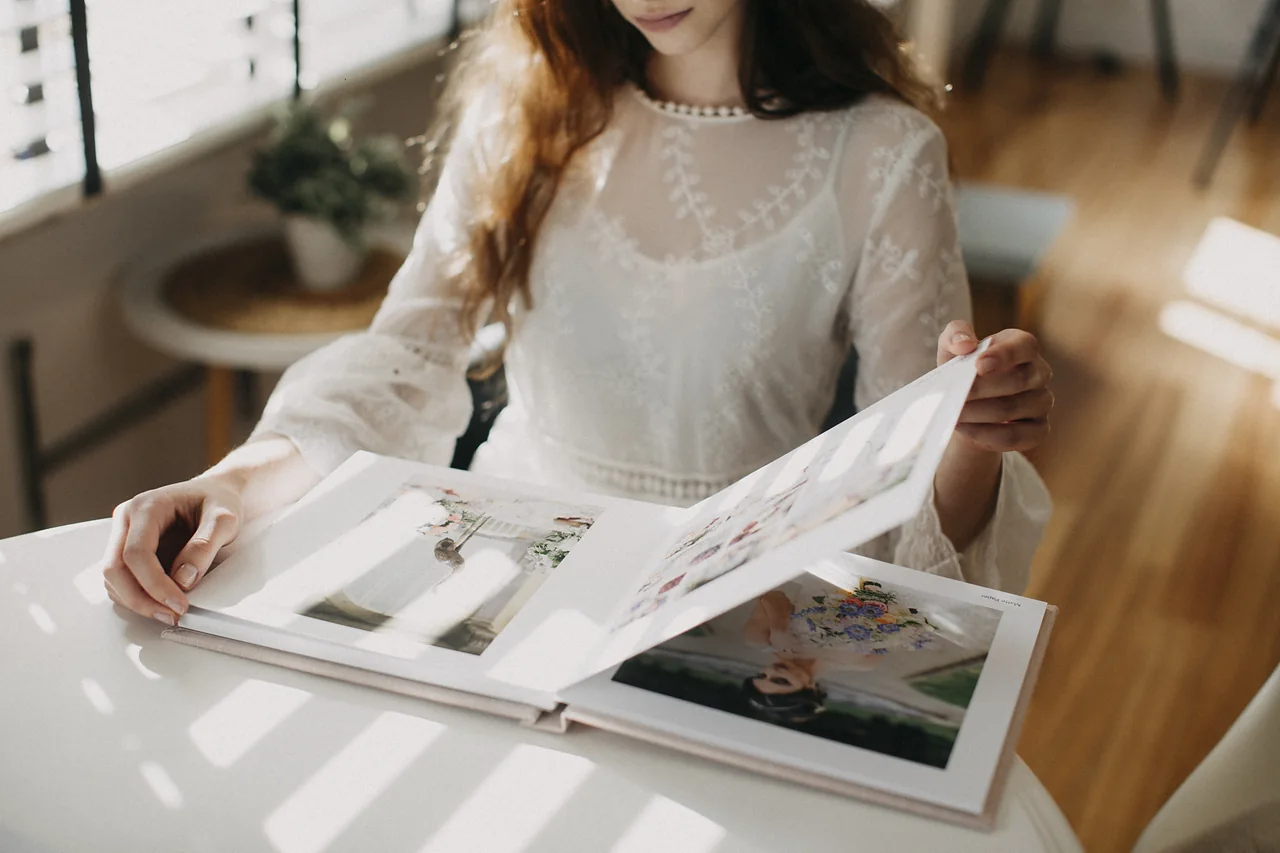 A woman turning a page of a lay-flat album lying open across the table